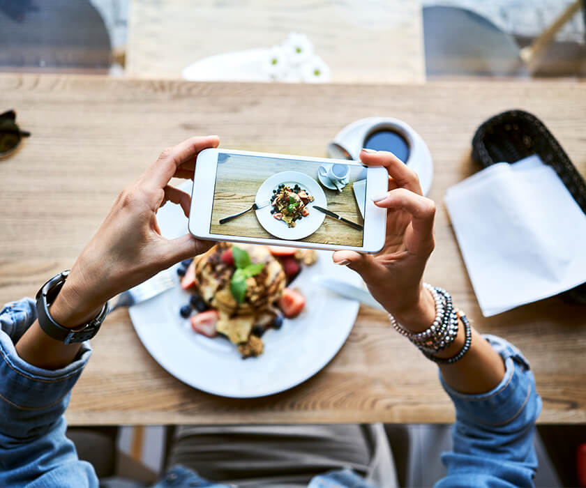 Women taking picture with an iPhone of a plate of pancakes placed on a wooden table 